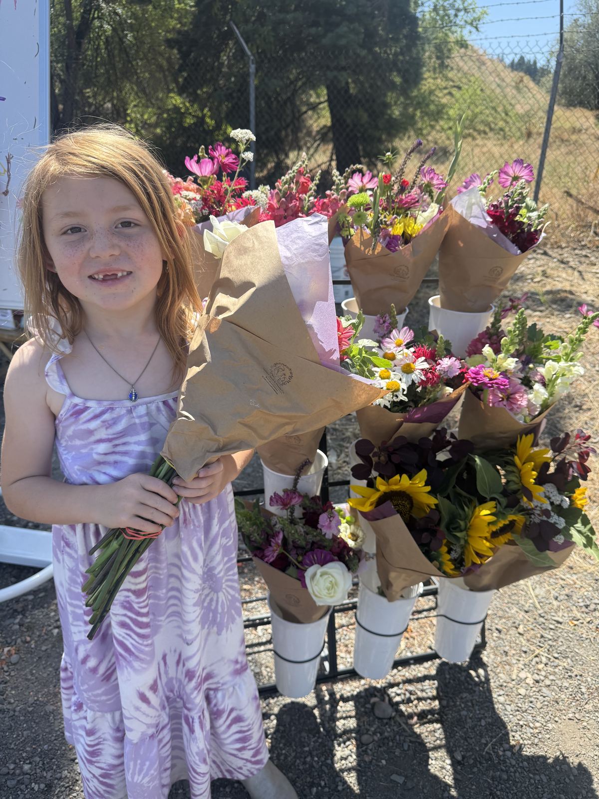 A young girl holding a hand-wrapped kraft paper bouquet in front of the full flower stand display.